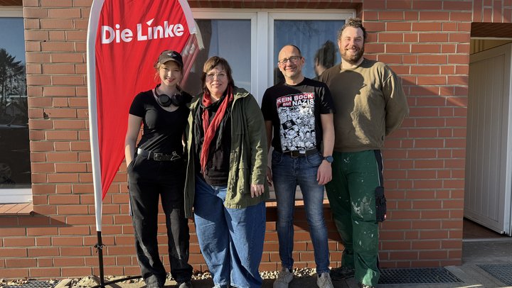 4 fröhliche Mitglieder der Partei Die Linke stehen Vor dem Eingang des neuen Büros in Buchholz